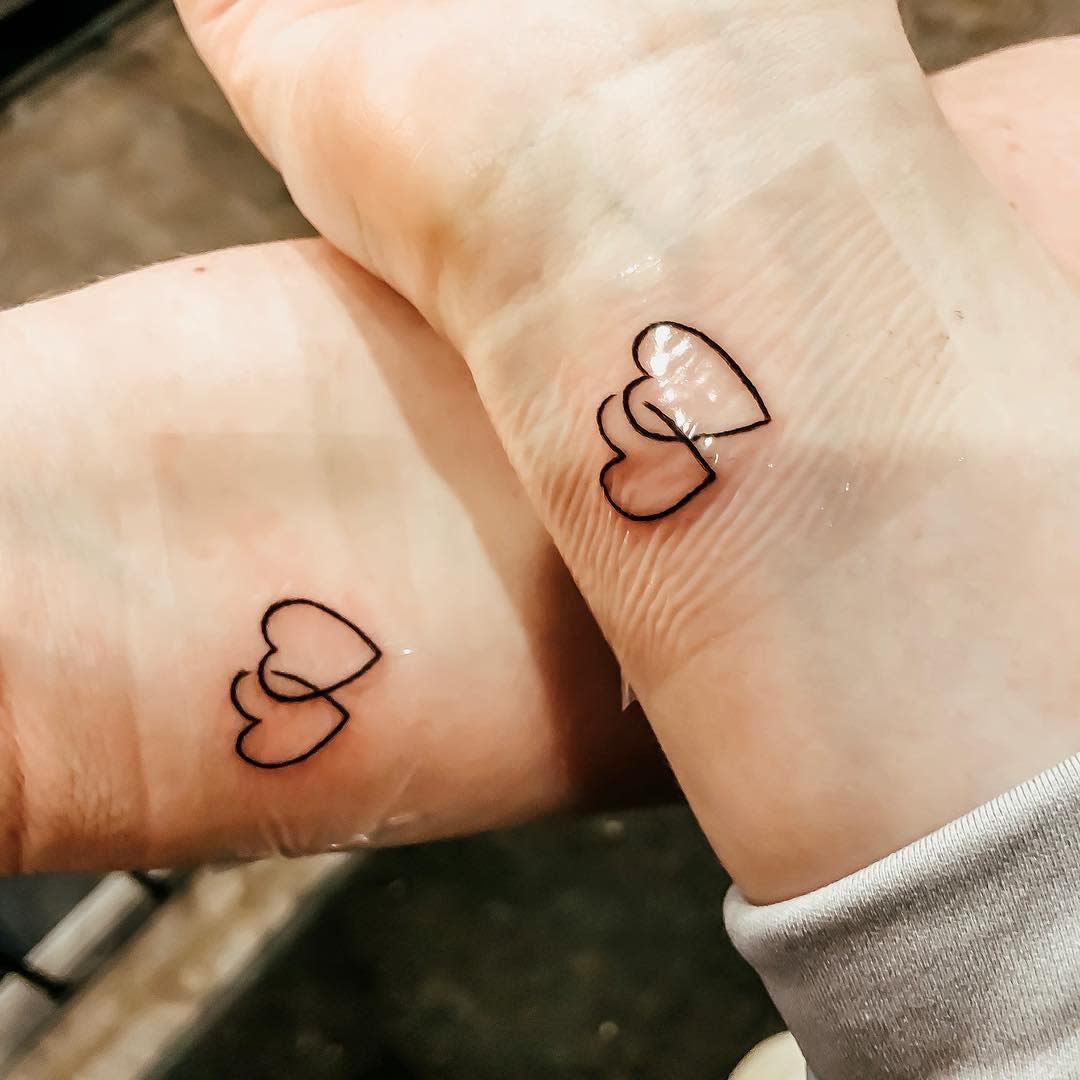 Two matching tattoos of interlocking hearts on two wrists